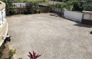 Un patio en la azotea con suelo de grava, rodeado por una cerca de madera y diversas plantas.