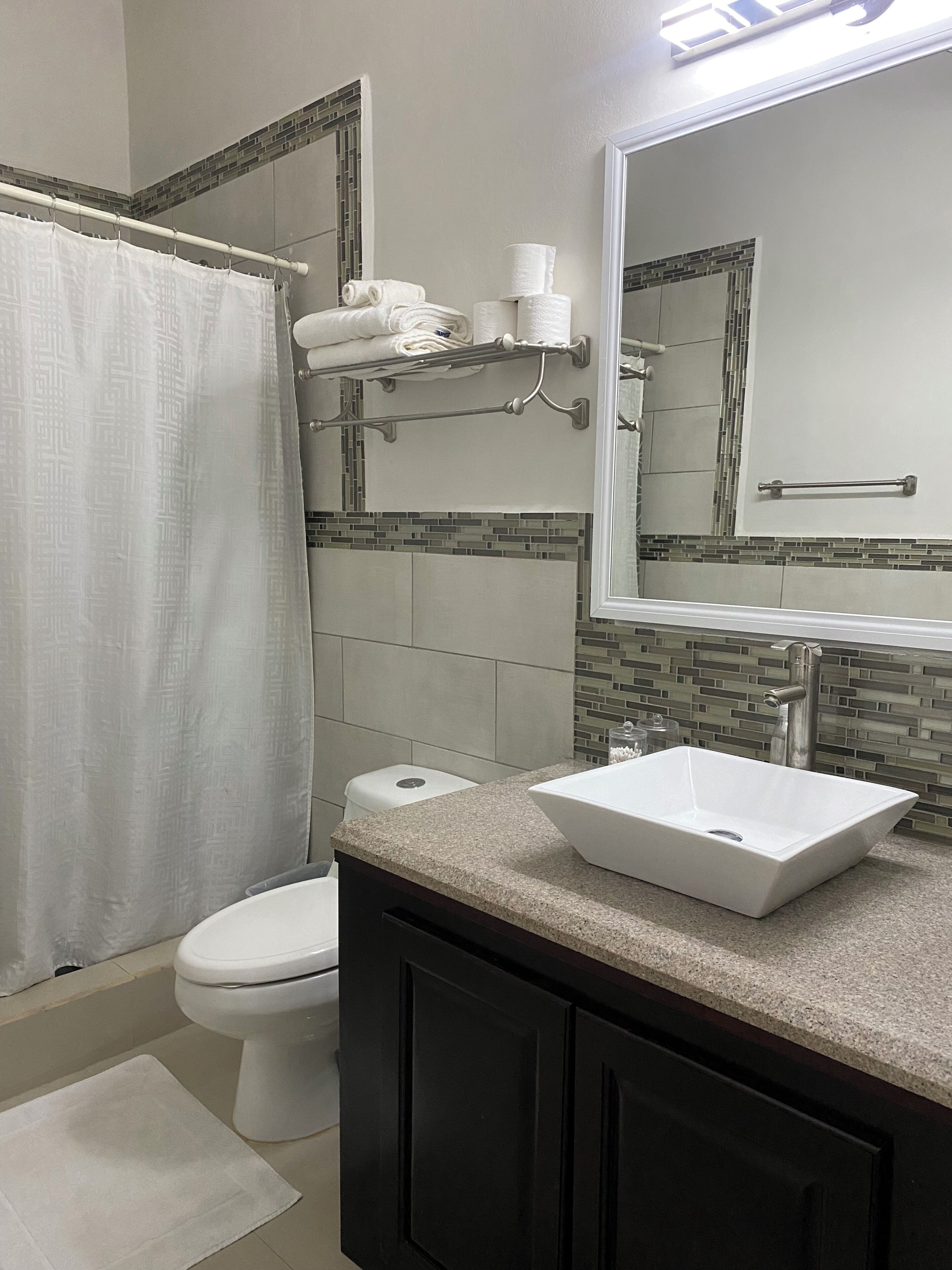 Un baño con inodoro, lavamanos y toallero con toallas y papel higiénico.