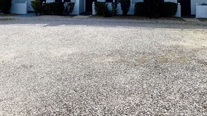 Monikerroksinen rakennus, jossa on parvekkeet, sorapäällysteinen ajotie ja kirkas taivas.