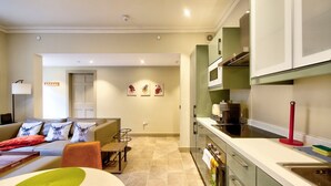 A modern apartment with a living room, kitchen, and dining area. There is a sofa with decorative pillows, a dining table with chairs, and a kitchen counter with a sink. - GuestReady - Manor Place Basement (Edinburgh)