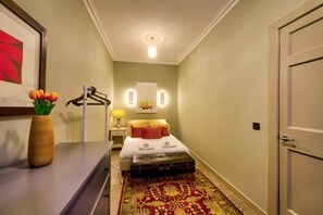 A hotel room with a bed, a bedside table with a lamp, a vase of flowers, and a rug. - GuestReady - Manor Place Basement (Edinburgh)