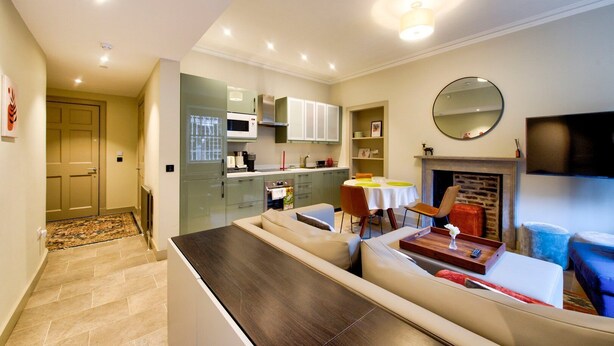 A modern kitchen with built-in appliances, a dining area with a round table and chairs, and a living area with a sofa and a fireplace. - GuestReady - Manor Place Basement (Edinburgh)
