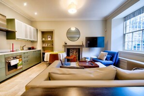 A modern living room with a sofa, a dining table, and a kitchen area with cabinets and a stove. - GuestReady - Manor Place Basement (Edinburgh)