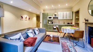 A modern living room with a grey sofa, a coffee table, and a dining area with a round table and chairs. - GuestReady - Manor Place Basement (Edinburgh)