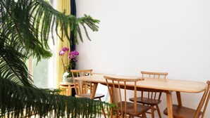 Un coin repas avec une table et des chaises en bois, une plante en pot aux feuilles vertes et une fenêtre avec des rideaux.