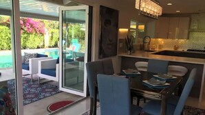 A modern kitchen with a dining area, featuring a glass door leading to a patio with outdoor furniture. - Mid-Century Private PoolSpa GolfResort LushGardens (New York)