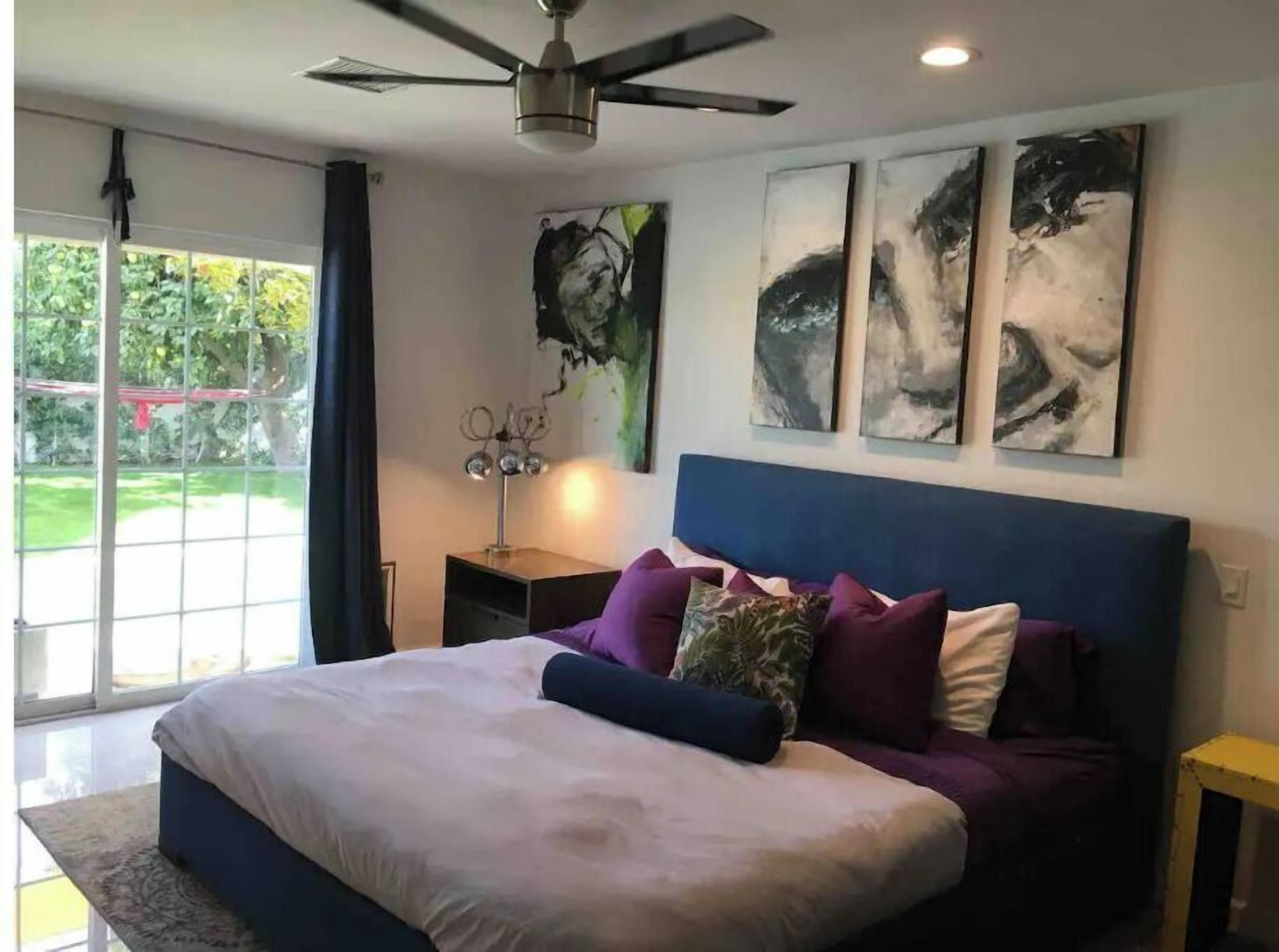 Een slaapkamer met een bed, een plafondventilator en kunst aan de muur.