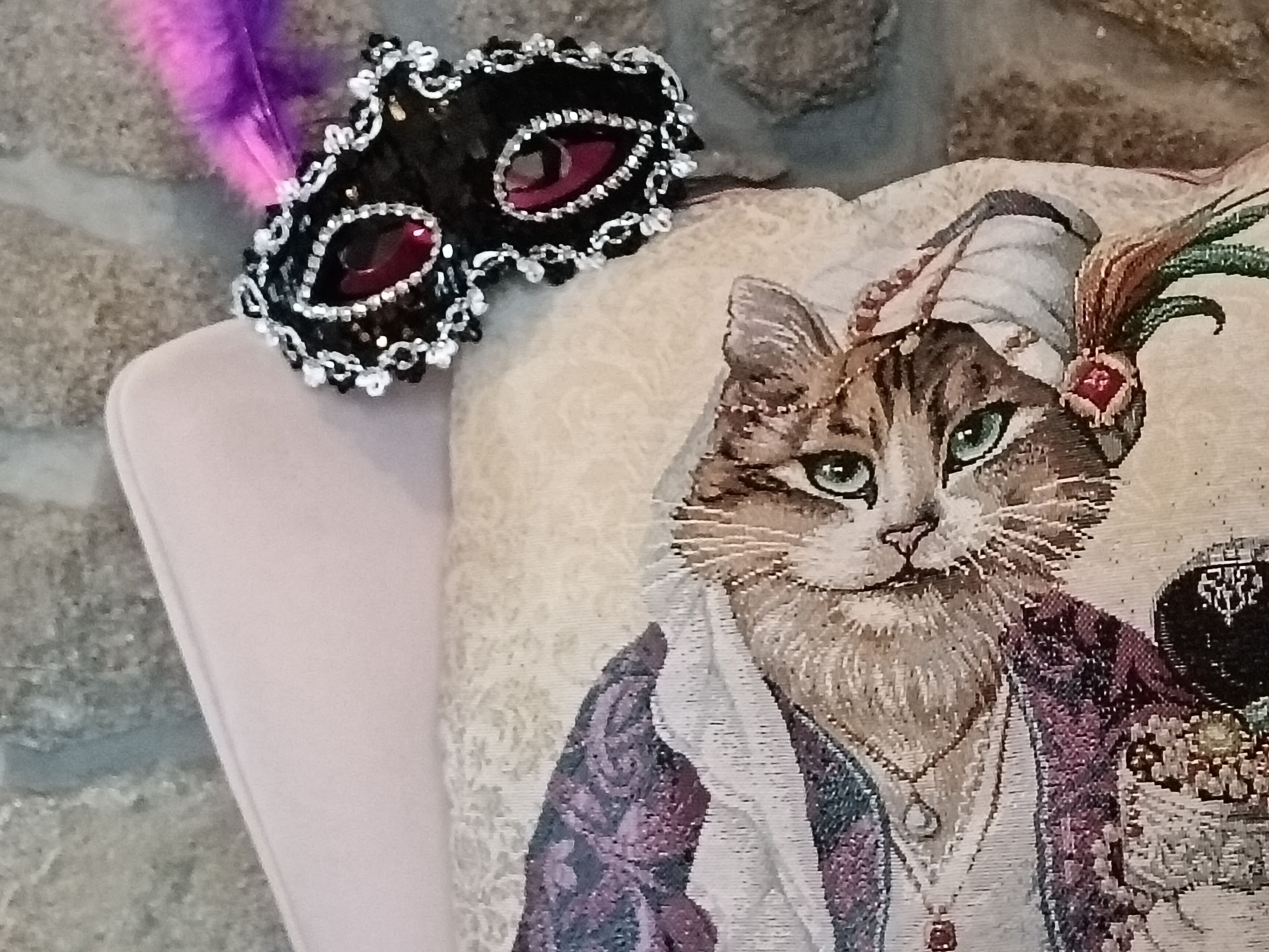 A plush toy cat with a decorative mask and feather on a white surface.