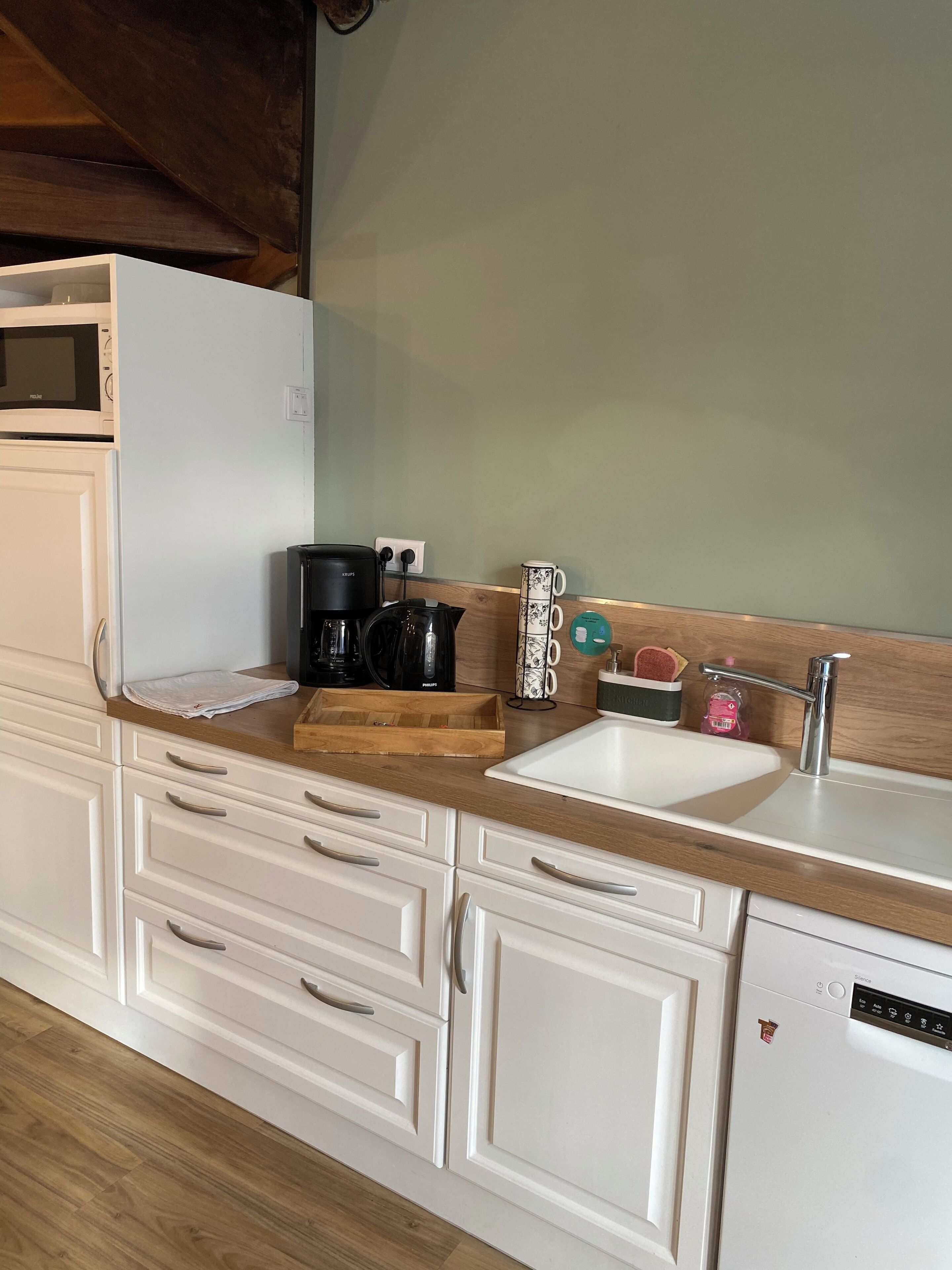 Una cucina con mobili bianchi, un piano di lavoro in legno, una macchina da caffè, un bollitore e una lavastoviglie.