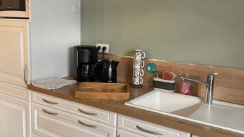 Una cucina con mobili bianchi, un piano di lavoro in legno, una macchina da caffè, un bollitore e una lavastoviglie.