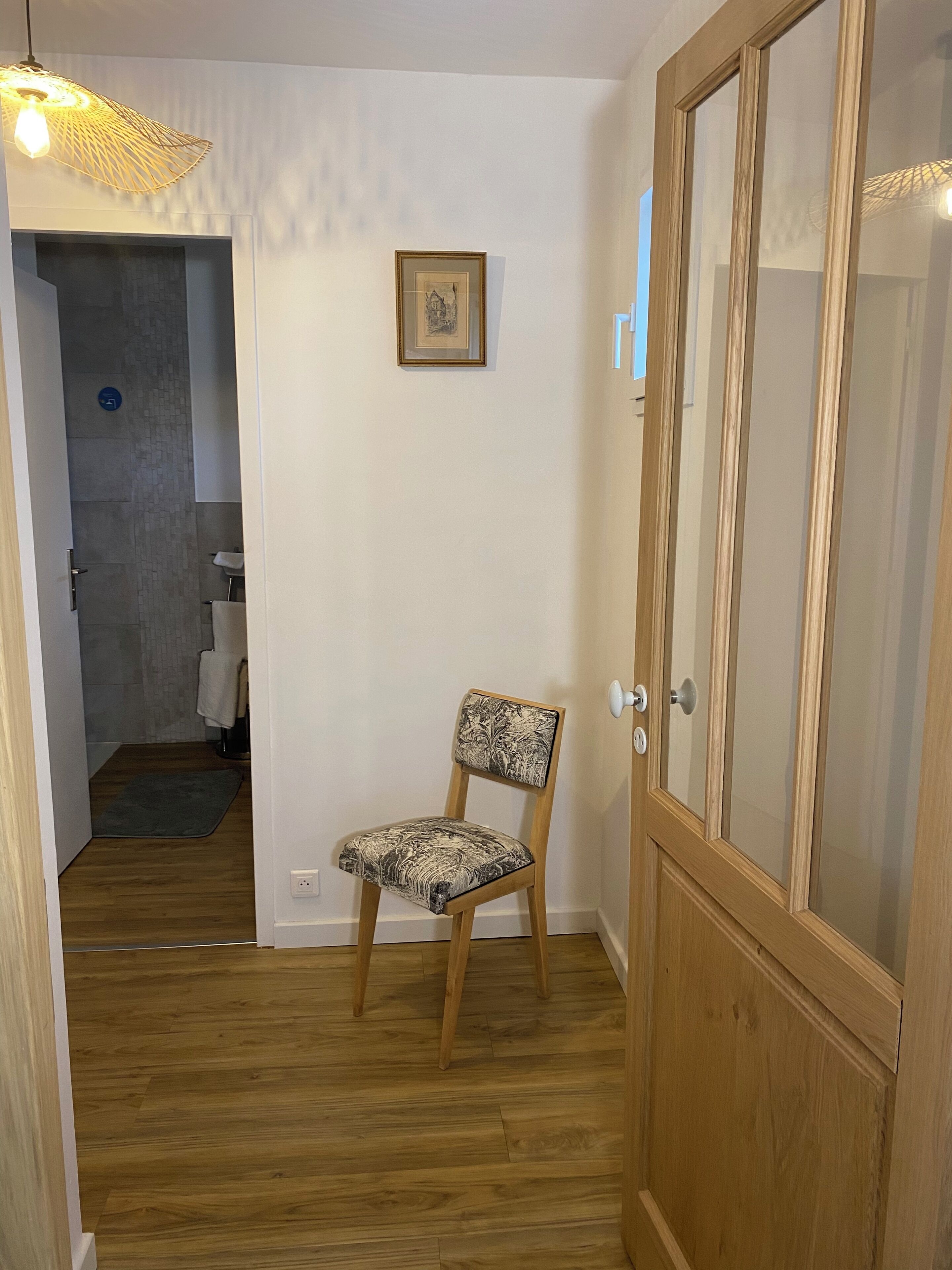 Une porte en bois avec des panneaux de verre, une chaise avec un coussin à motifs et un tableau encadré au mur.