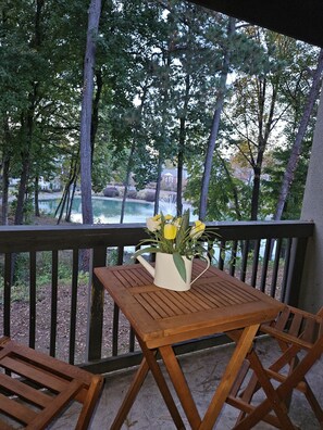 A wooden table and chairs on an outdoor deck with a view of a lake and trees.