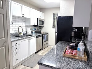 A modern kitchen with white cabinets, a granite countertop, stainless steel appliances, and a coffee maker.