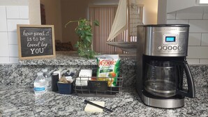 Eine Küchenarbeitsplatte mit Kaffeemaschine, einem Schild, einer Pflanze und Küchenutensilien.