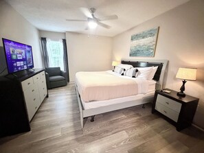 A hotel room with a bed, a desk, a chair, a TV, and a ceiling fan.