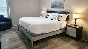 Ein Schlafzimmer mit Bett, Nachttischen, Deckenventilator, Fenster und einem Bild an der Wand.