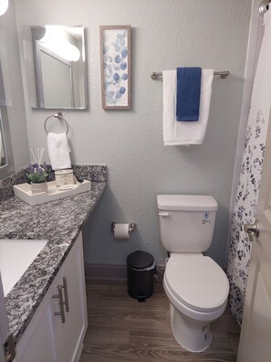 A bathroom with a toilet, sink, and mirror. There are towels and a trash can.
