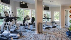 Ein Fitnessstudio mit verschiedenen Cardiogeräten, großen Fenstern und einem gemusterten Teppich.