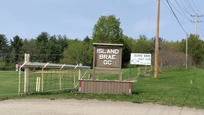 A sign for Island Brae Golf Club with a wooden structure and a fenced area.