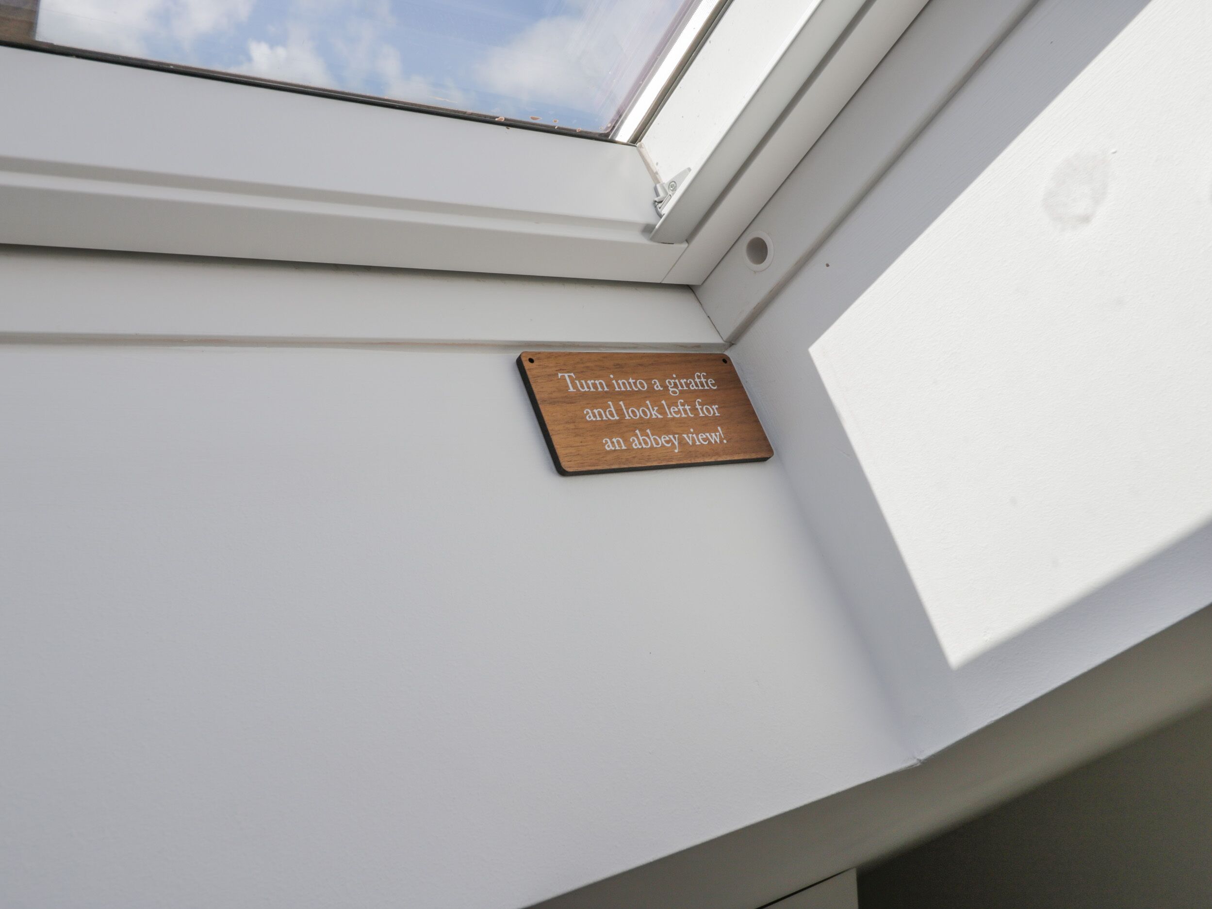 Un tragaluz con una placa de madera que dice '¡Conviértete en una jirafa y mira a la izquierda para ver una abadía!'