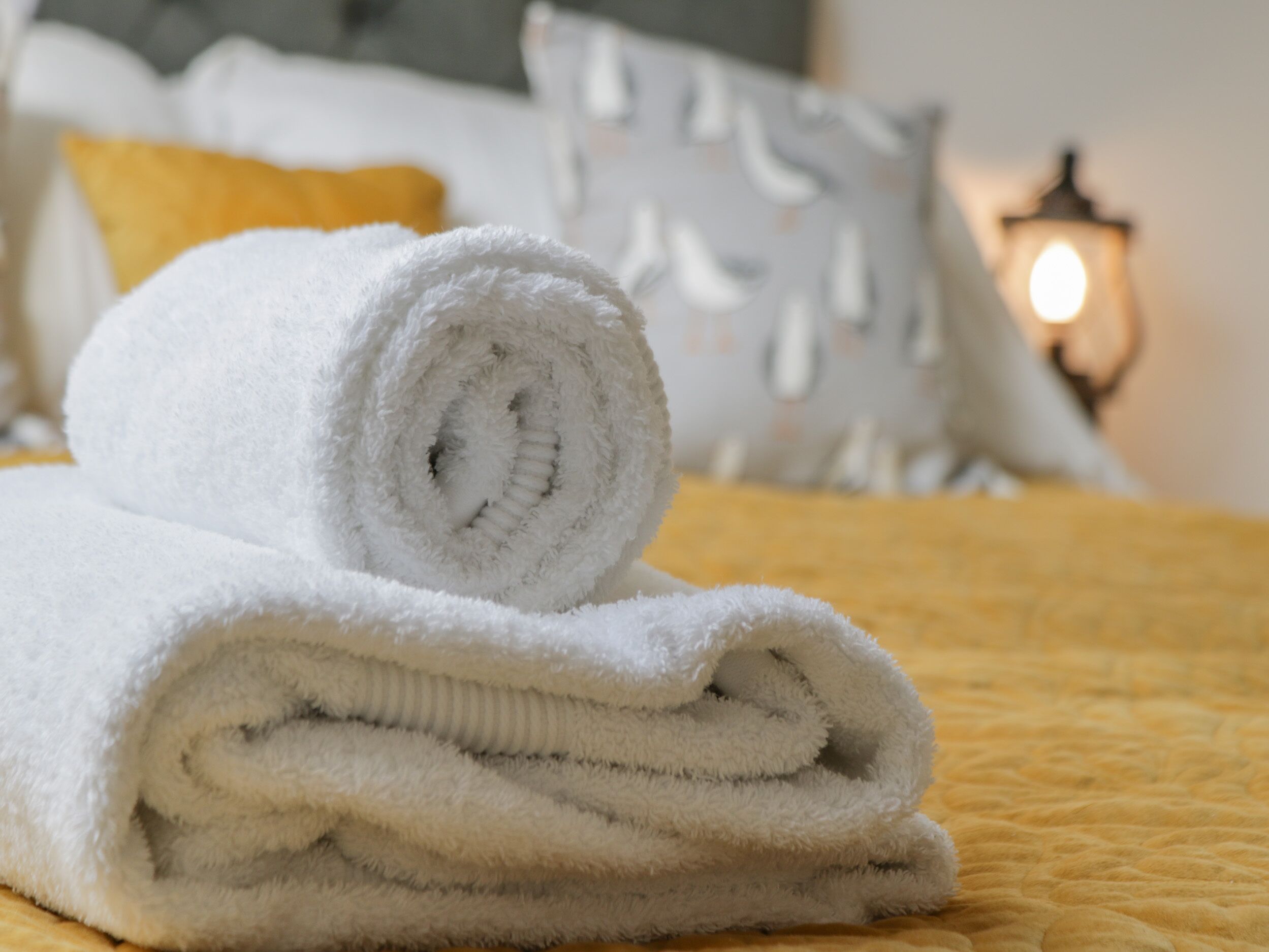 A neatly folded white towel on a bed with a yellow quilt.