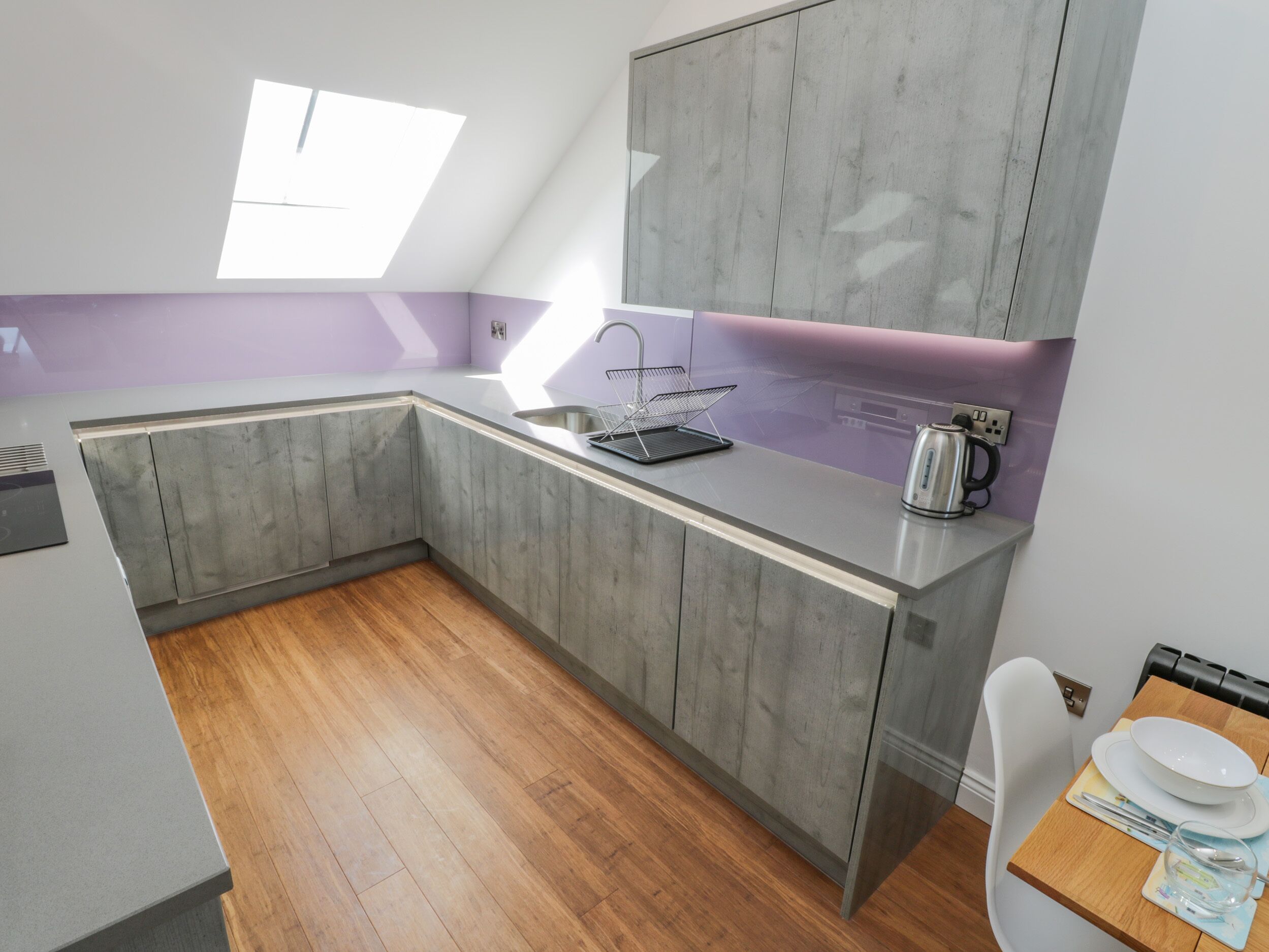 A modern kitchen with grey cabinets, a white countertop, and a window providing natural light.
