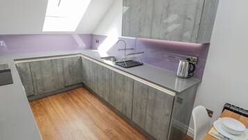 A modern kitchen with grey cabinets, a white countertop, and a window providing natural light.