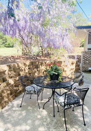 An outdoor patio with a round table and four chairs, surrounded by a stone wall and a wisteria tree. - 7th Ave Manor, Remodeled 1930’s Manor just minutes from Historic Downtown Laurel (Laurel)