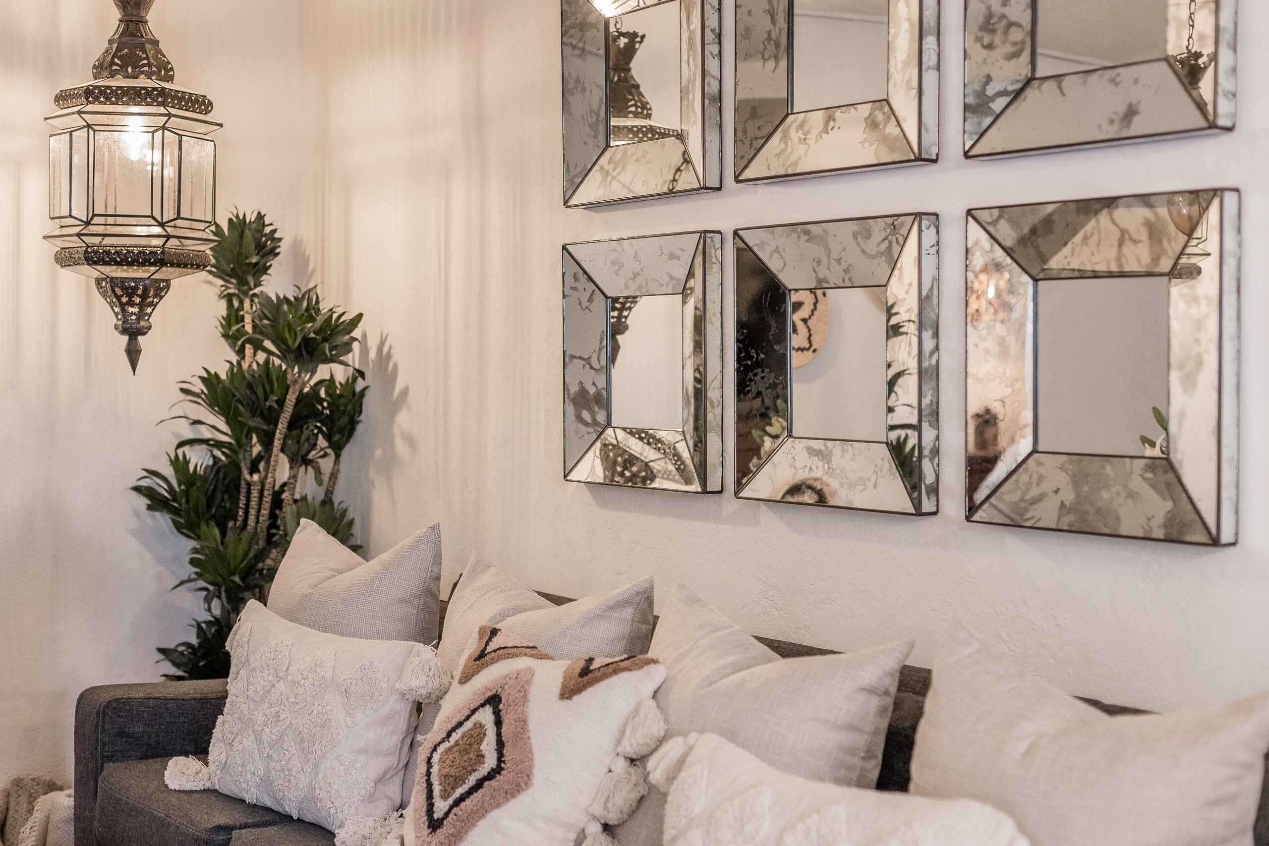 Ein Wohnzimmer mit grauem Sofa, mehreren Kissen, einem hängenden Laternen und einem Blumentopf.