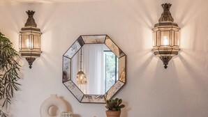A wall-mounted hexagonal mirror with a geometric frame, flanked by two wall-mounted lantern-style lights.