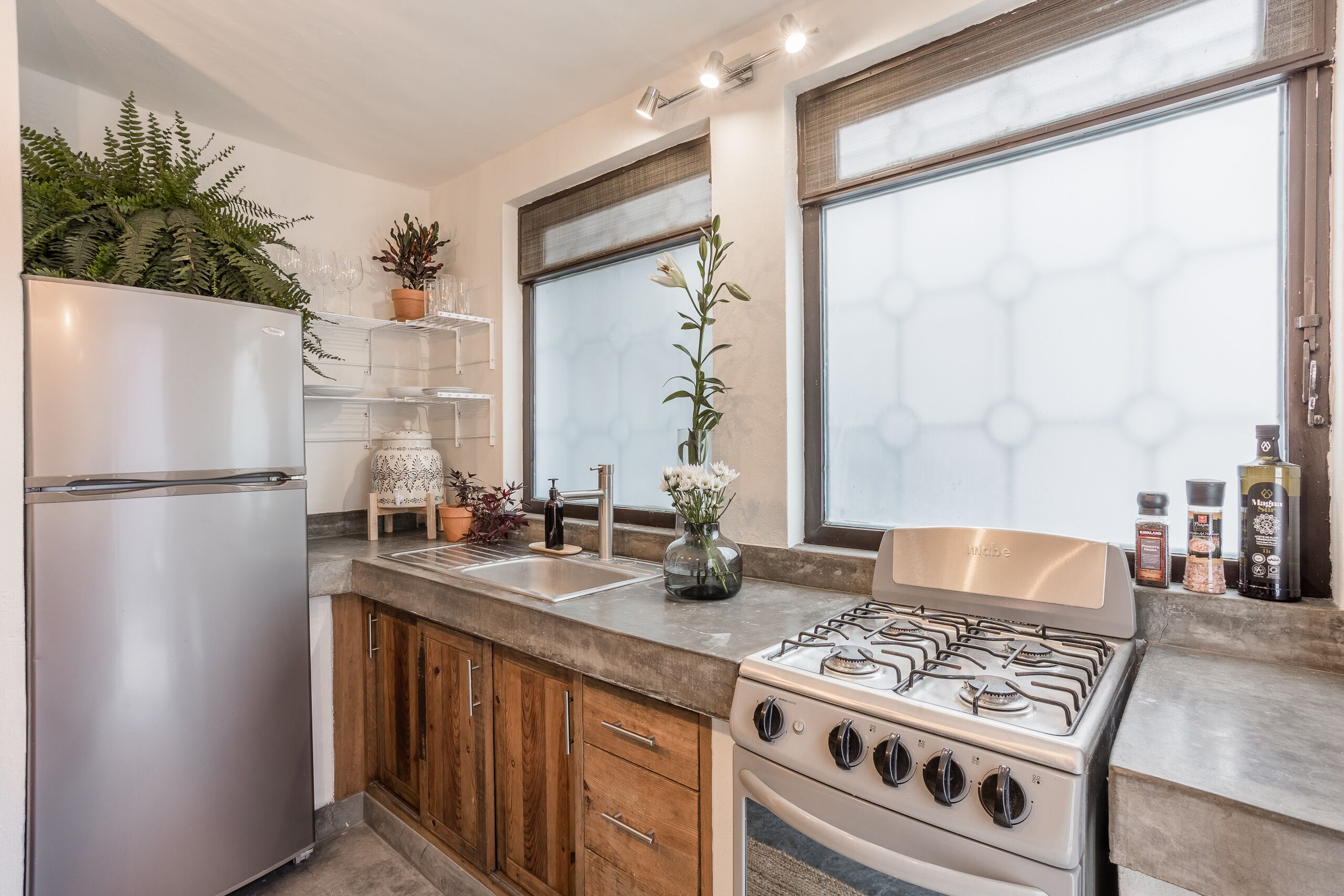 A modern kitchen with a stainless steel refrigerator, wooden cabinets, a gas stove, and a window with a hexagonal pattern.