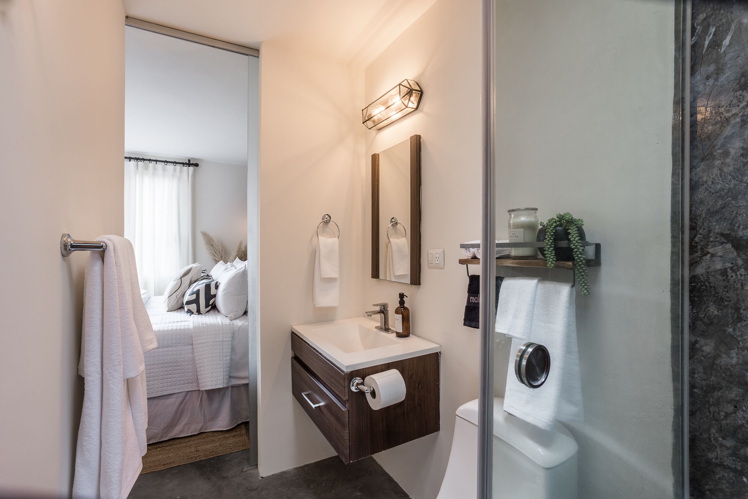 A modern bathroom with a shower, a toilet, and a sink with a mirror above it. There is a towel rack and a small shelf with toiletries.