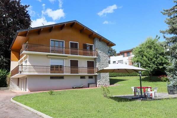 A two-story building with a balcony, a stone chimney, and a small lawn area with outdoor furniture.