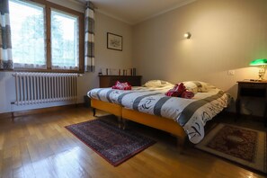 A bedroom with a bed, a radiator, a window with curtains, a bedside lamp, and a rug. - Vintage (Annecy-le-Vieux)