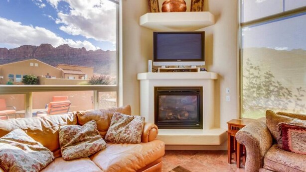 Una sala de estar con chimenea, televisión y ventanas amplias que ofrecen vistas a la montaña.
