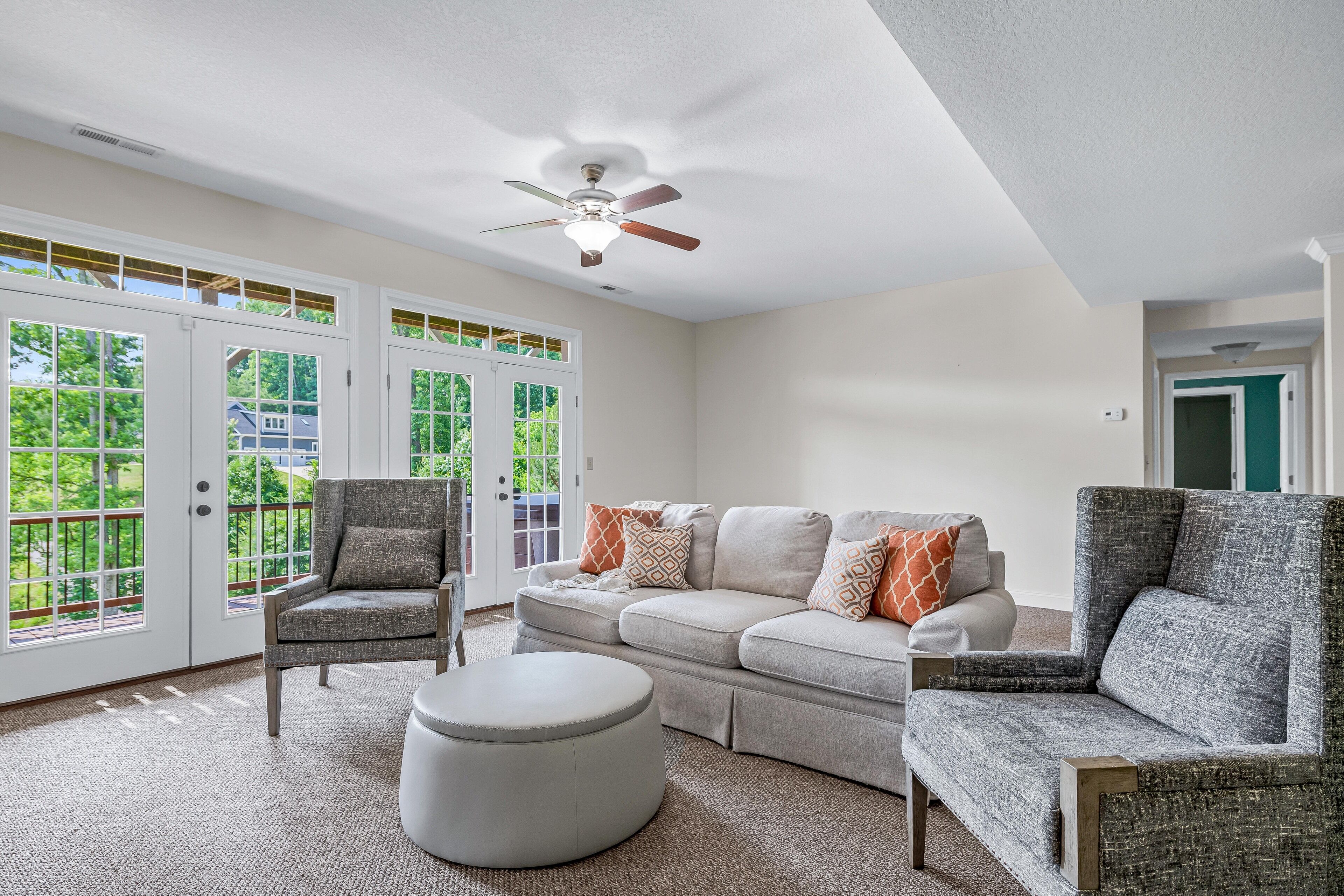 A spacious living room with a large window, a ceiling fan, and a grey sectional sofa.
