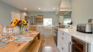 A modern kitchen with white cabinets, a wooden dining table set for six, and a built-in oven. - Achanlochan Farm (Taynuilt)