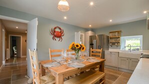 A dining area with a wooden table set for four, a crab decoration on the wall, and a kitchen in the background. - Achanlochan Farm (Taynuilt)