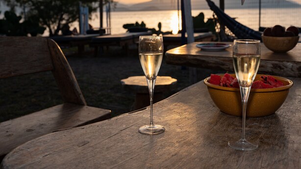 Deux verres de vin blanc sur une table en bois, accompagnés d’un bol rempli de tranches de pastèque.