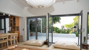 Un intérieur moderne comprenant un coin repas, une porte vitrée donnant sur un jardin et un espace salon confortable agrémenté de coussins.