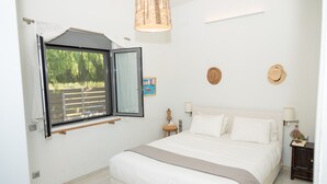 Une chambre avec un grand lit, une fenêtre donnant sur un paysage verdoyant, un luminaire au plafond et une petite table de chevet avec une lampe.