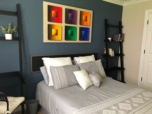 A bedroom with a bed, pillows, a bookshelf, and a wall art piece.