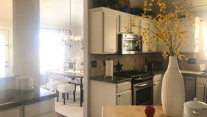 Una cocina con armarios blancos, una estufa y un lavamanos. Hay un jarrón con flores amarillas en la encimera.