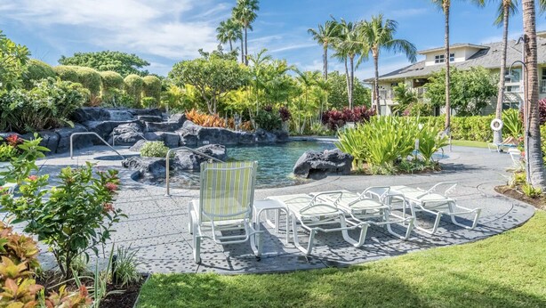 A resort pool area with a waterfall, palm trees, and lounge chairs.