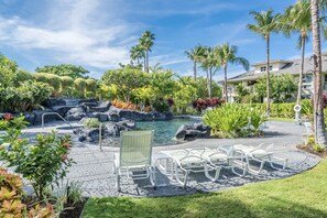 A resort pool area with a waterfall, palm trees, and lounge chairs.