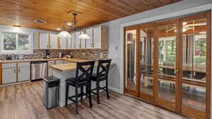 A modern kitchen with wooden cabinets, a central island, and a large sliding glass door leading to an outdoor area. - Spacious home minutes from Gunstock and Lake Winnipesaukee (Gilford)