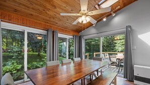 A spacious room with a large wooden table, comfortable seating, large windows, and a ceiling fan. - Spacious home minutes from Gunstock and Lake Winnipesaukee (Gilford)
