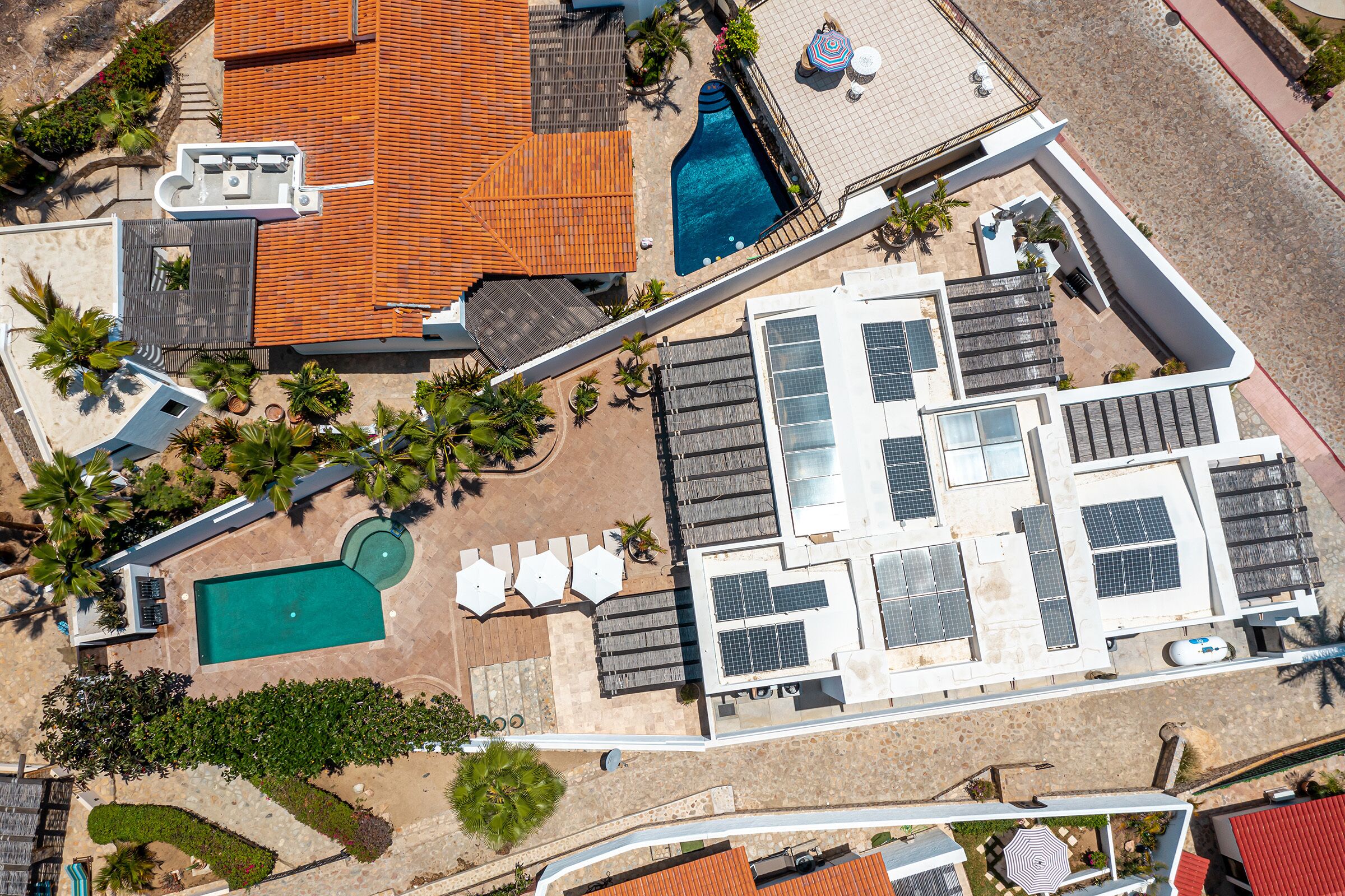 Vue aérienne d’une propriété dotée d’une piscine, de chaises longues, d’un patio couvert et de panneaux solaires.