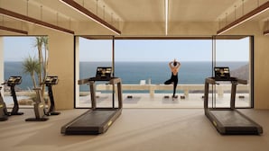 A modern gym with two treadmills, a yoga mat, and a view of the ocean.
