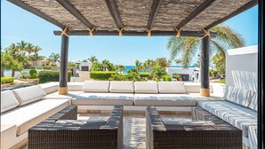 A covered outdoor seating area with a view of the sea, featuring wicker furniture and a pergola.